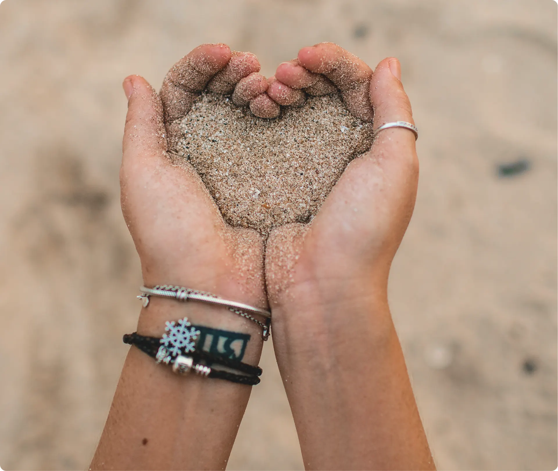 Hands holding sand in shape of heart.