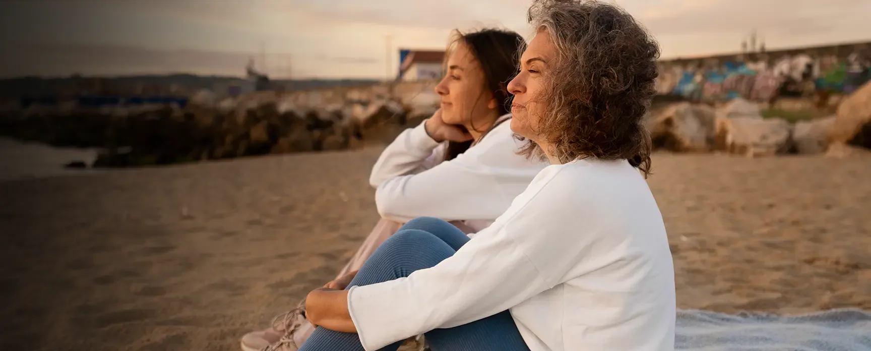 A mother and daughter sitting together on the beach at sunset.