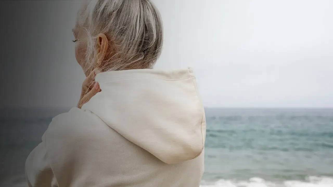 Woman in a cream hoodie looking out over the ocean.