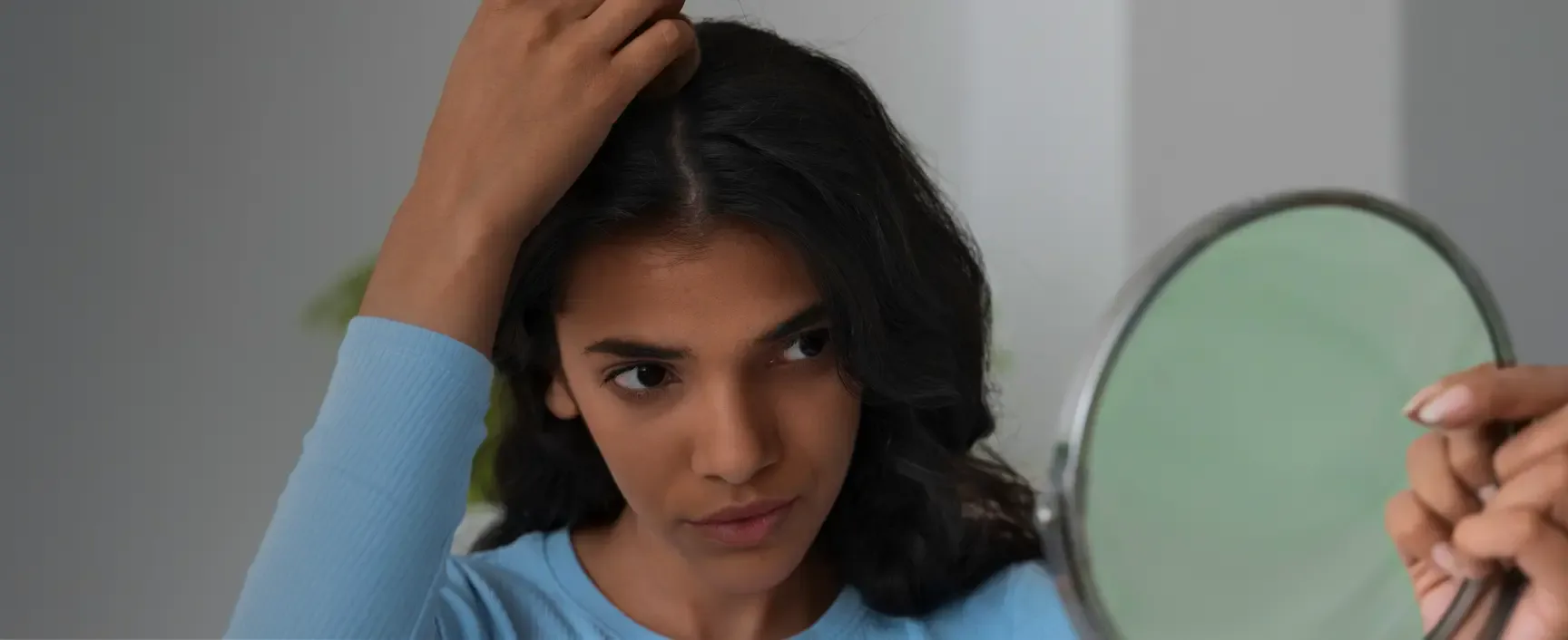 Woman examining her hairline in a hand mirror.
