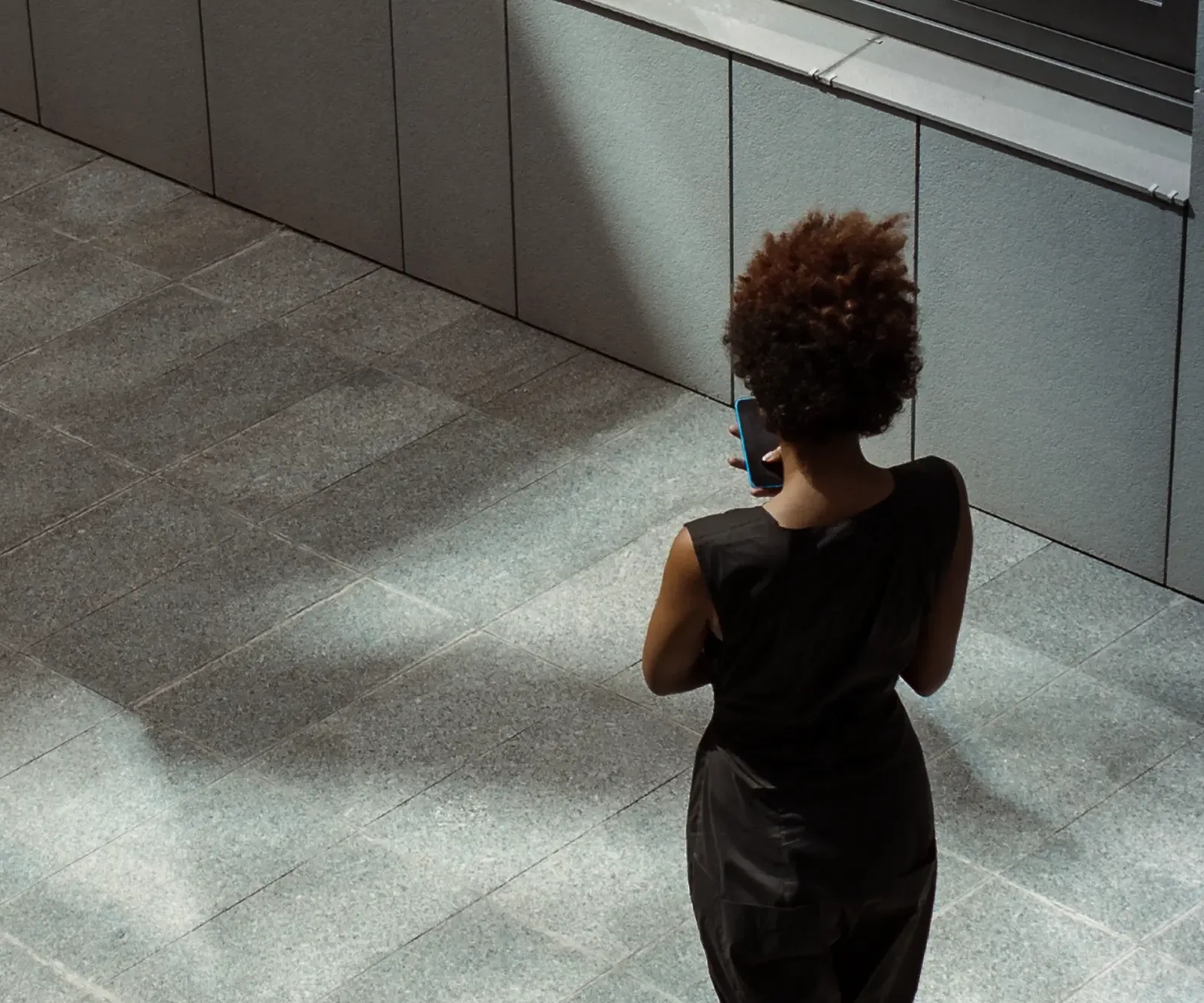 A woman walking across a sunlit stone plaza.
