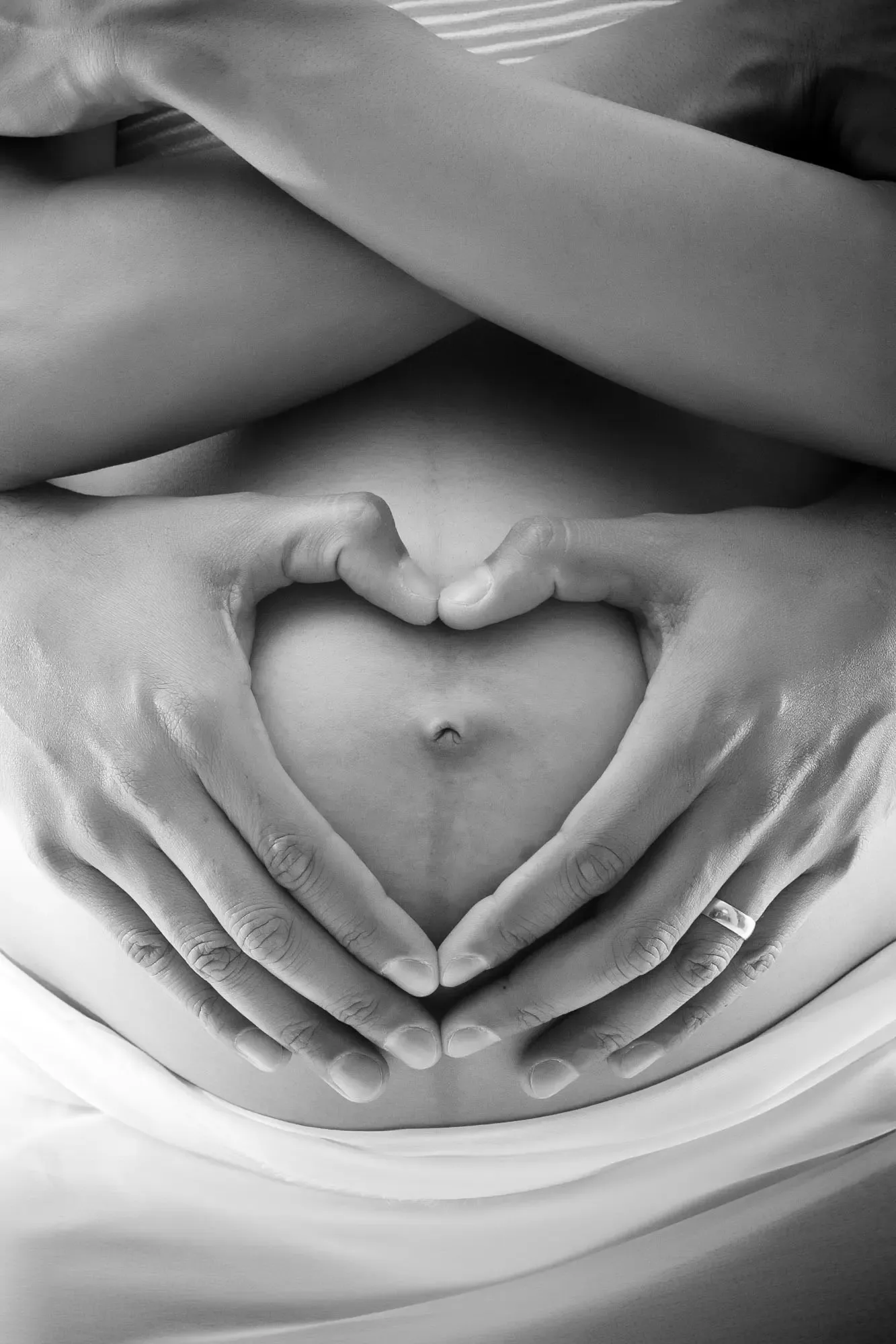 A woman's hands forming a heart over her pregnant belly.