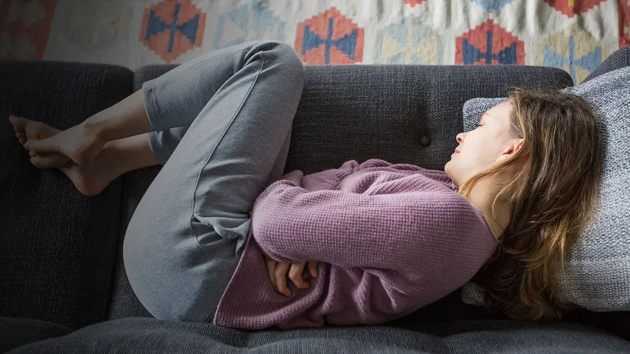 Woman curled up on a couch holding her stomach in discomfort.
