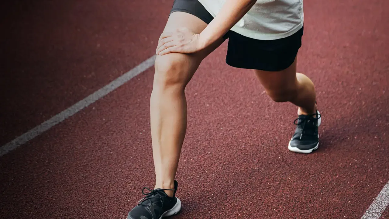 Runner stretching on a track, resting a hand on their knee.