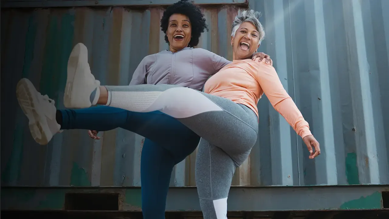 Two women laughing together while exercising outdoors.