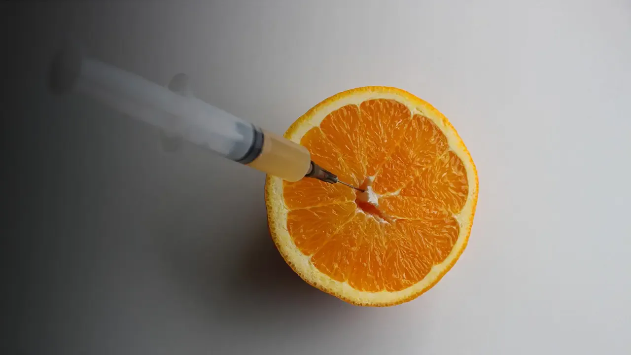 A syringe drawing juice from a fresh orange half.